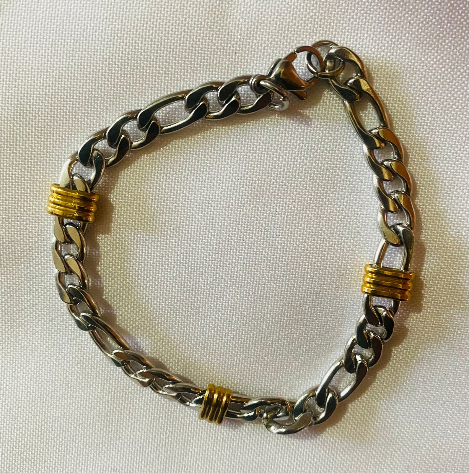 Una pulsera de cadena de plata y oro está sobre una tela blanca.