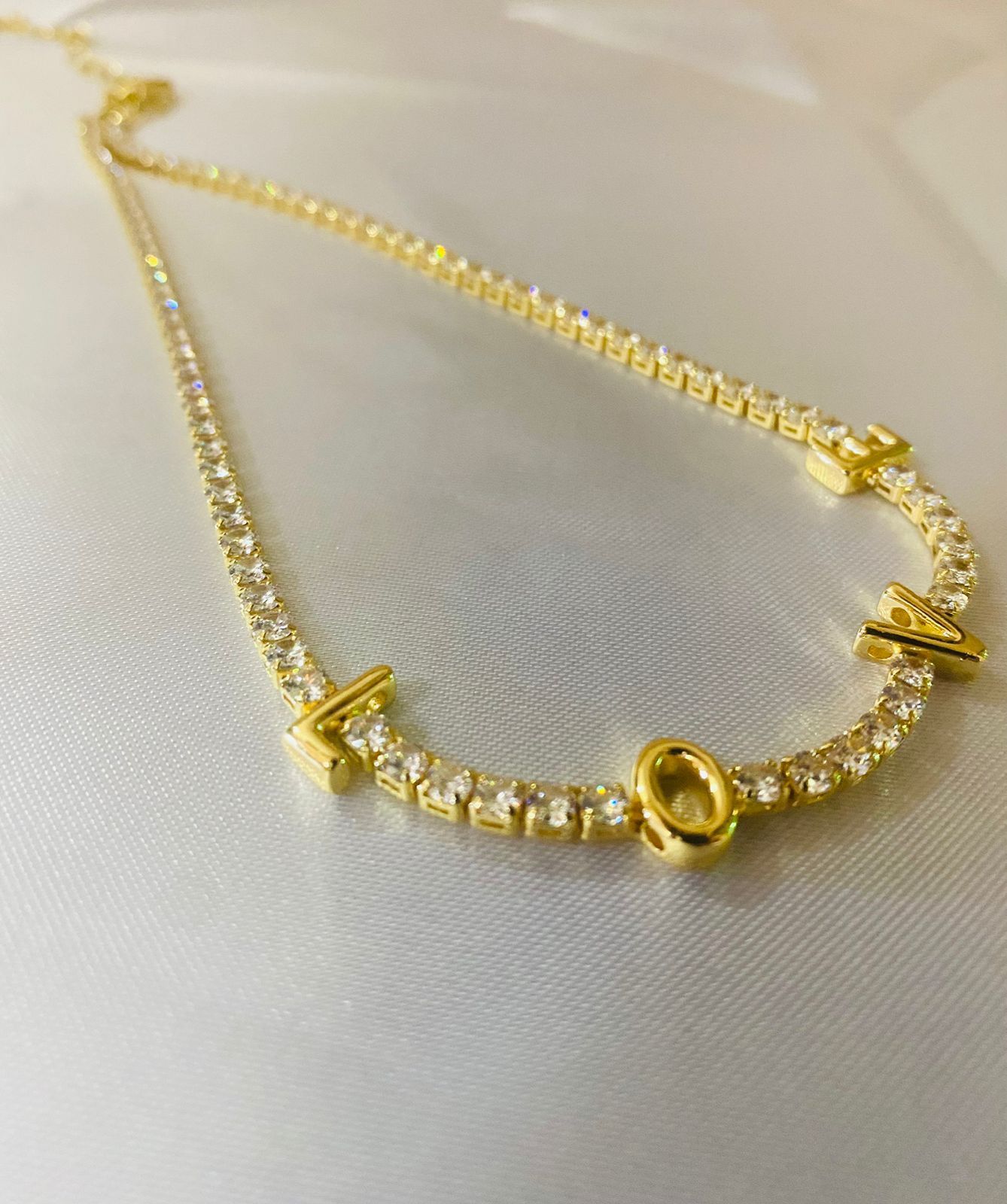 Un collar de oro con una letra o está sobre una superficie blanca.