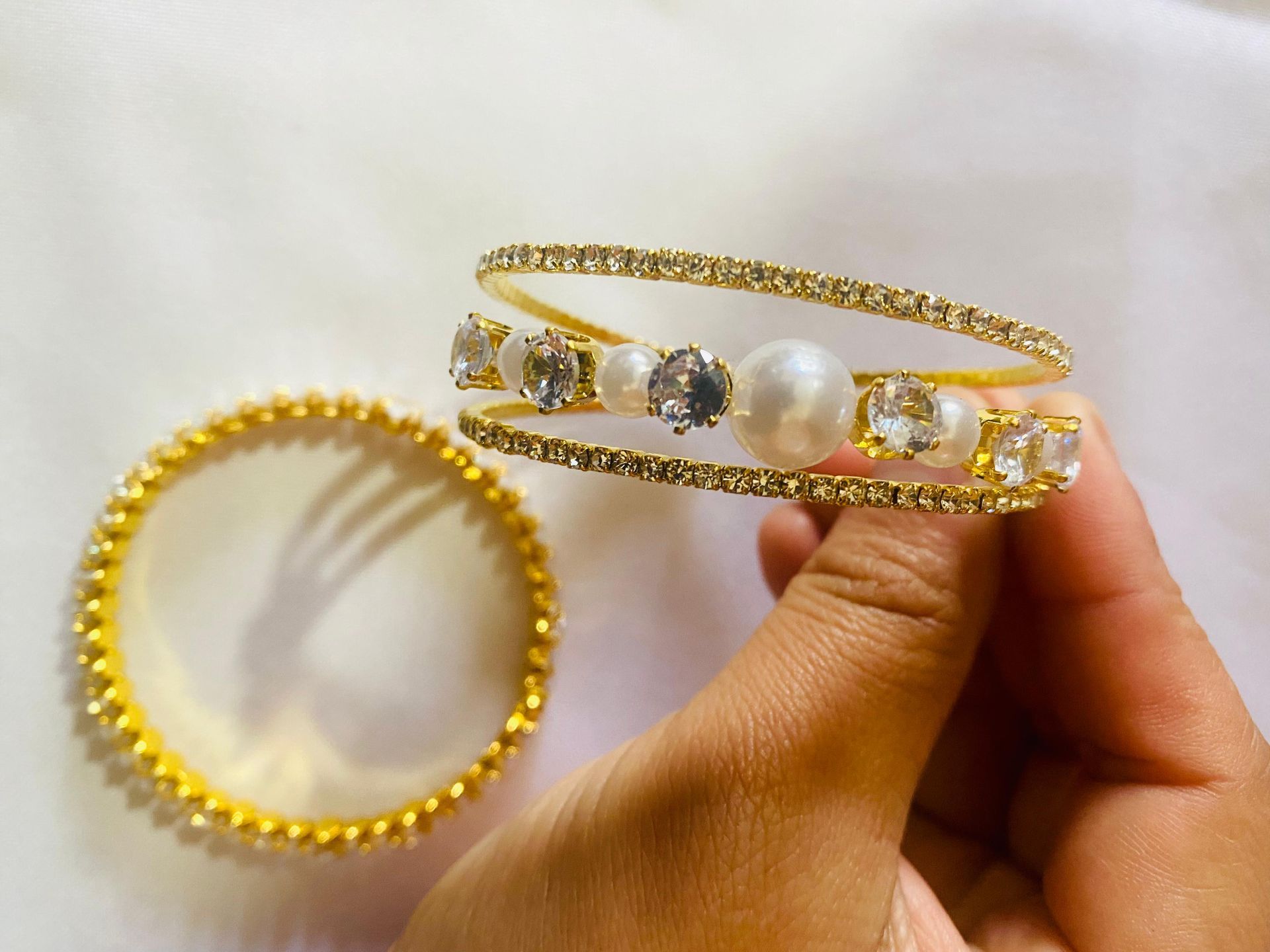 Una persona sostiene una pulsera de oro con perlas y diamantes de imitación.