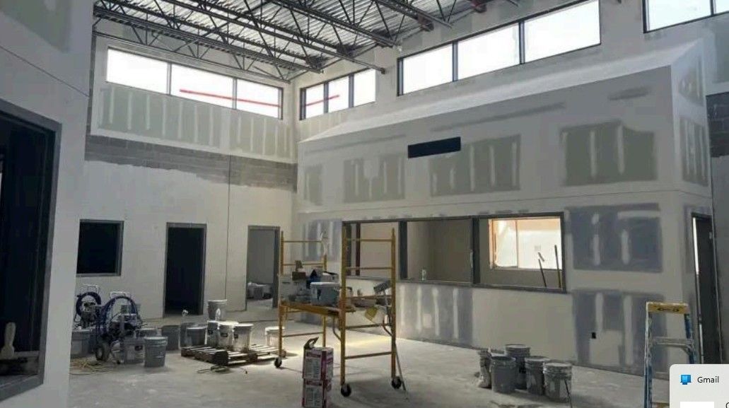 Interior of a building under construction with drywall, scaffolding, and tools in a bright open room