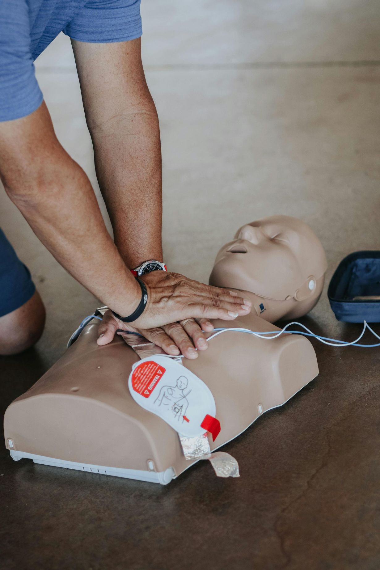 Person performing CPR chest compressions on a training mannequin with AED pads attached