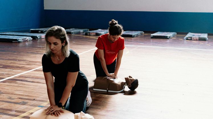 Two people practicing CPR on training mannequins in a gymnasium-like room.