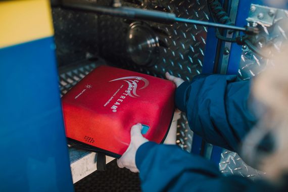 Person placing a red defibrillator case on a metal shelf in a vehicle or emergency response compartment