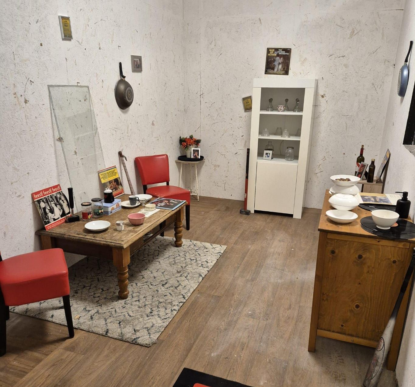 Een kleine leefruimte met een rode stoel, salontafel en houten kast. De muren zijn getextureerd.