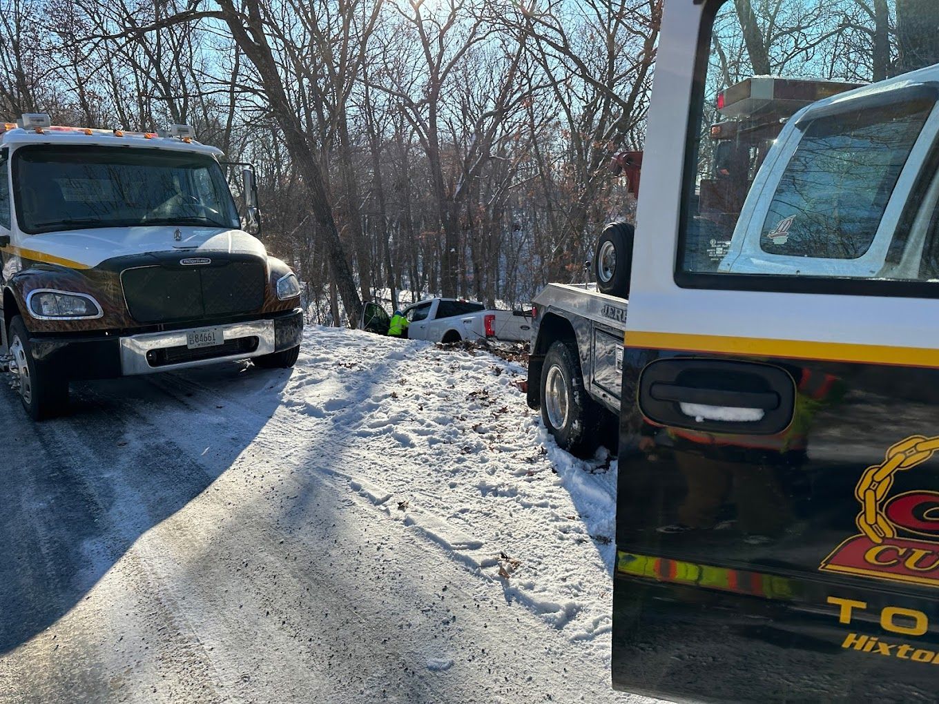 Two tow trucks are parked on the side of a snow covered road.