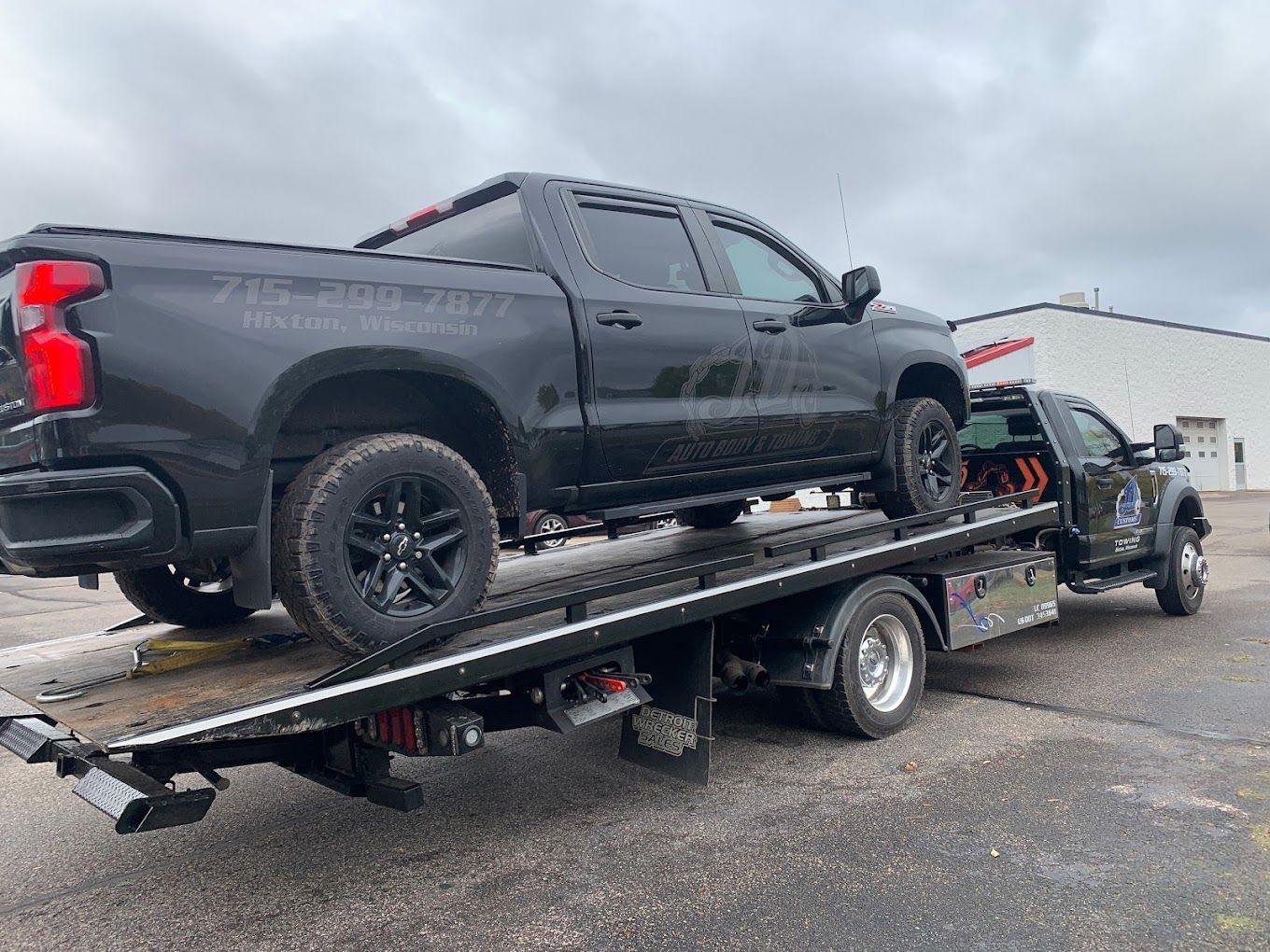 A black truck is being towed by a tow truck.