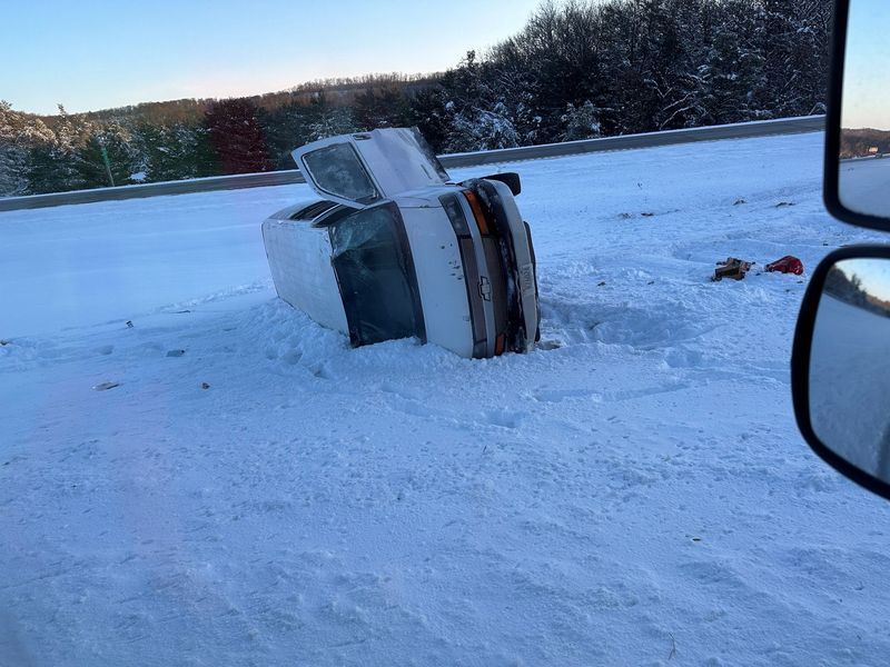A car is turned over in the snow on the side of the road.