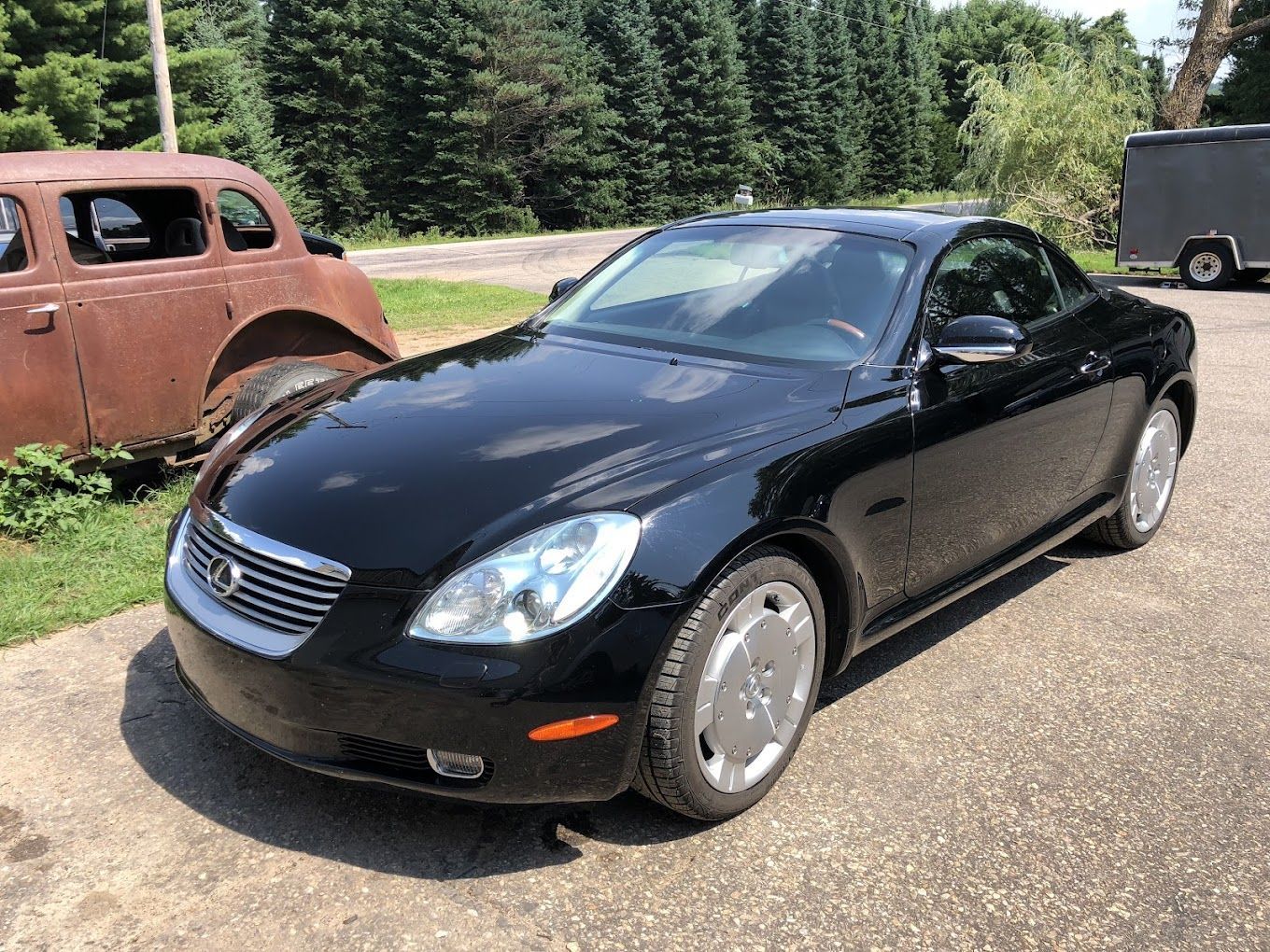 A black sports car is parked on the side of the road next to a rusty car.