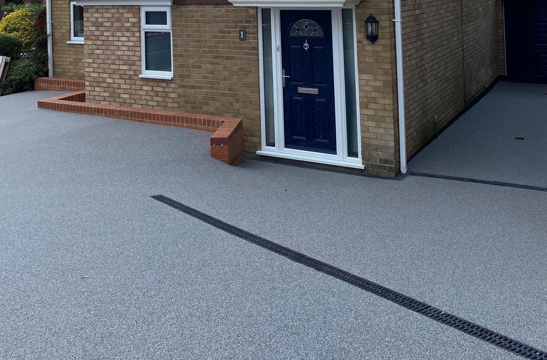 A brick house with a blue door and a gravel driveway in front of it.