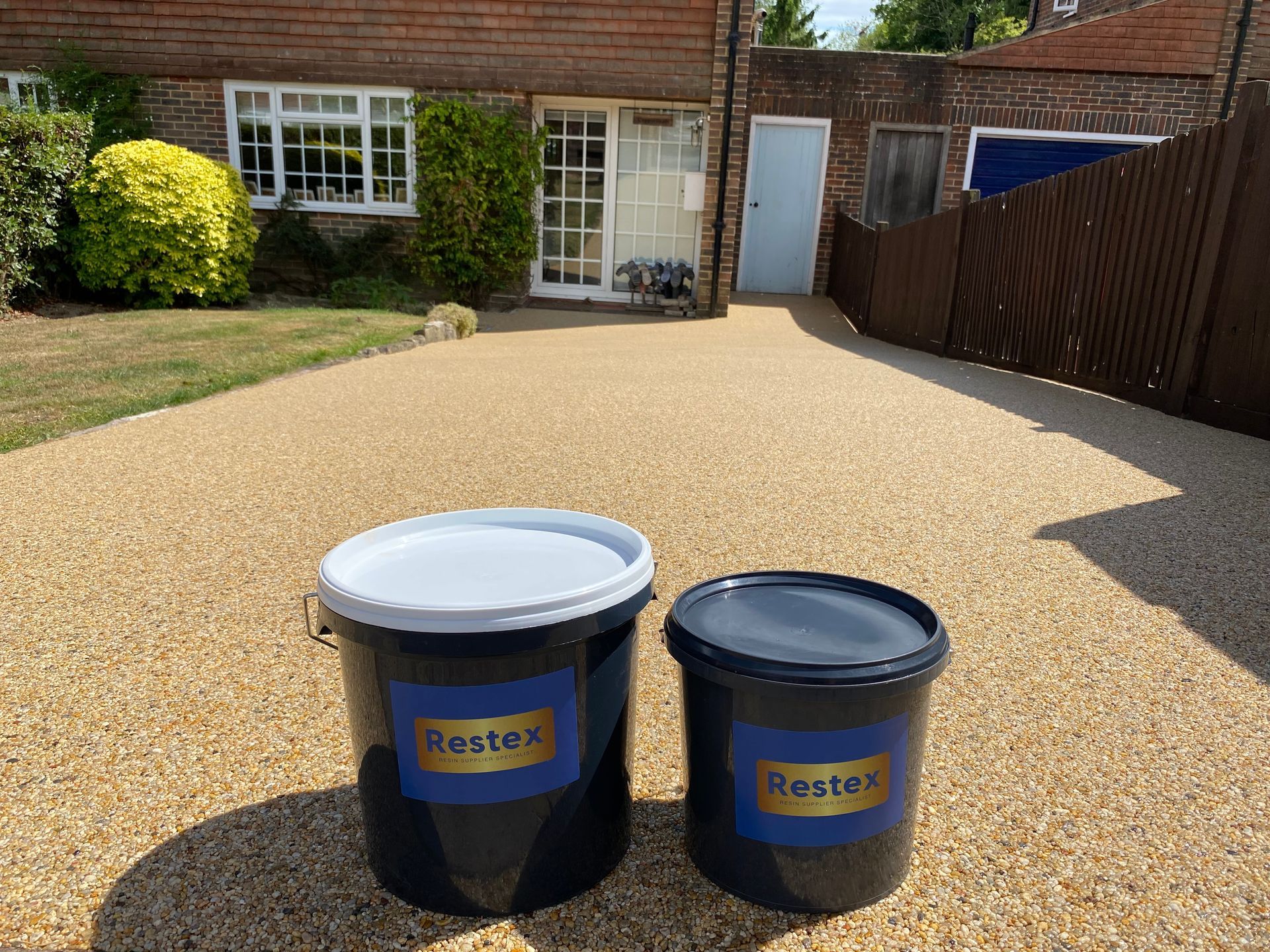 Two buckets of luxury restex resin bound  are sitting on a gravel driveway in front of a house.

