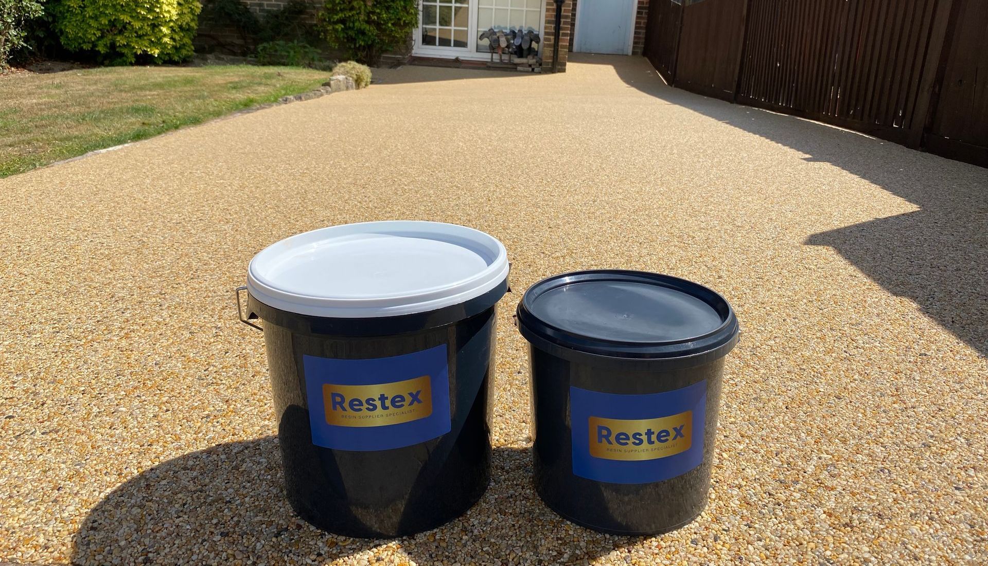 Two buckets of restex are sitting on top of a golden resin bound driveway.Restex