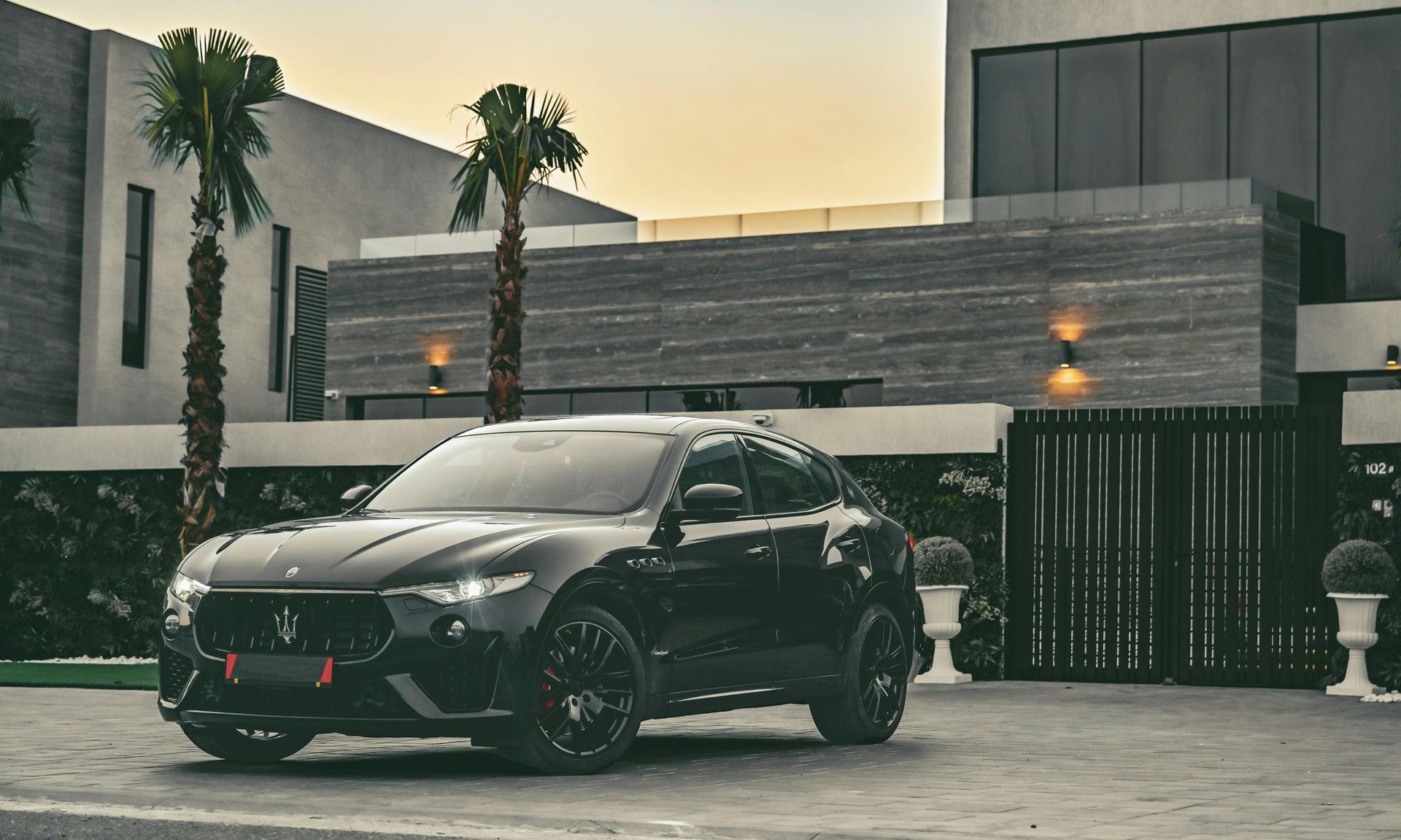 A black car is parked in front of a house with palm trees.