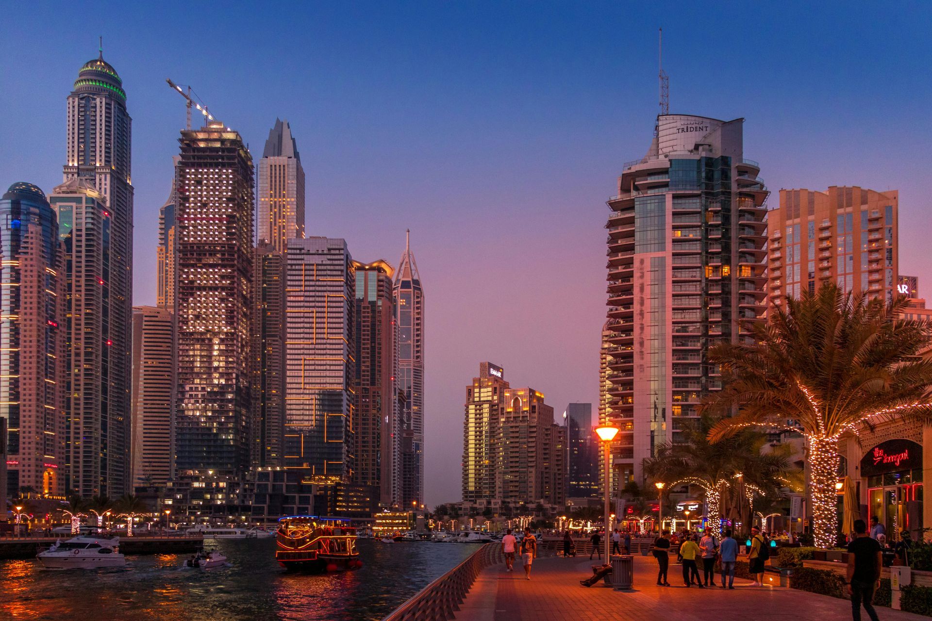 A group of people are walking down a sidewalk in front of a city skyline at night.