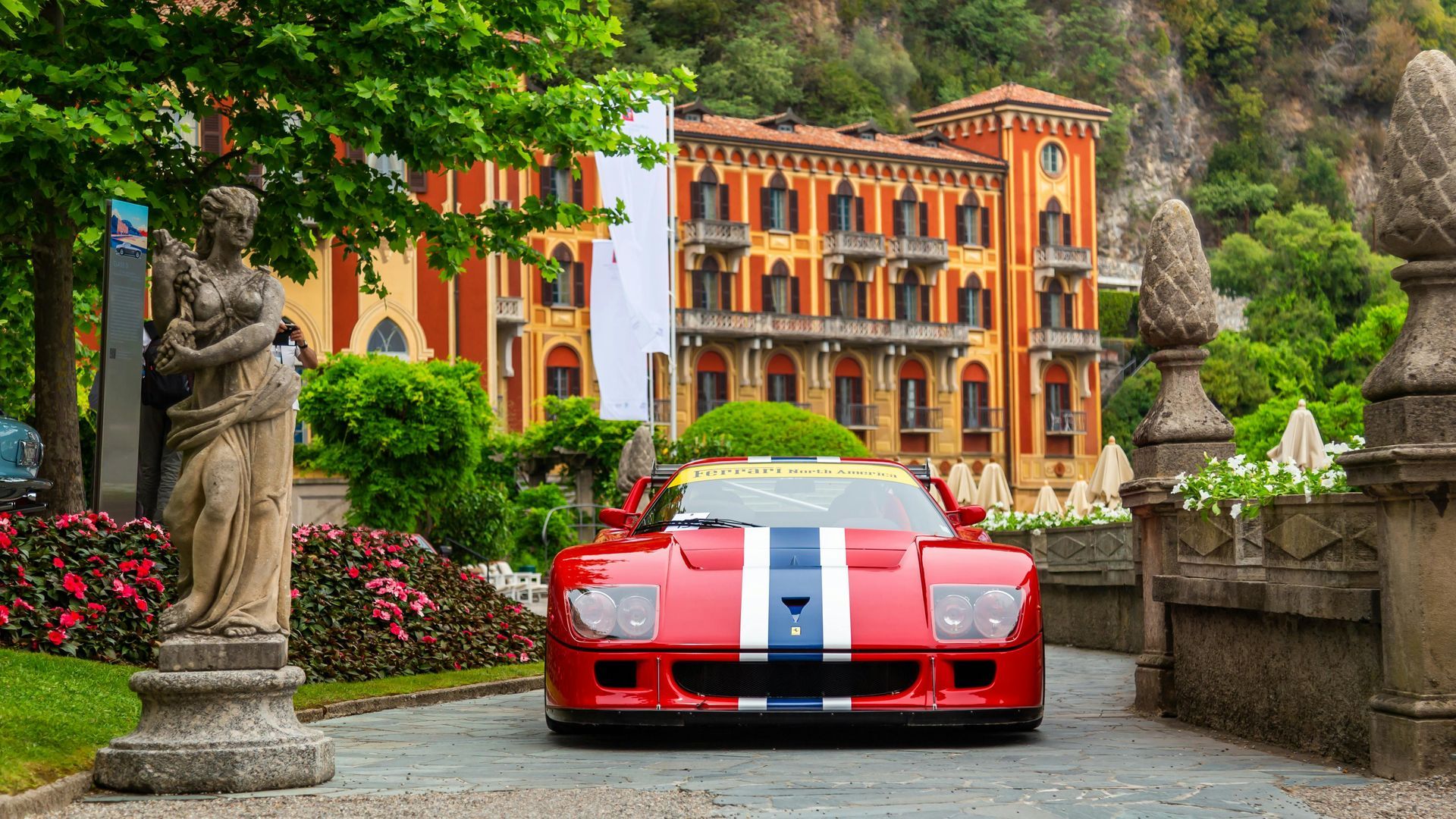 A red sports car is driving down a road in front of a building.