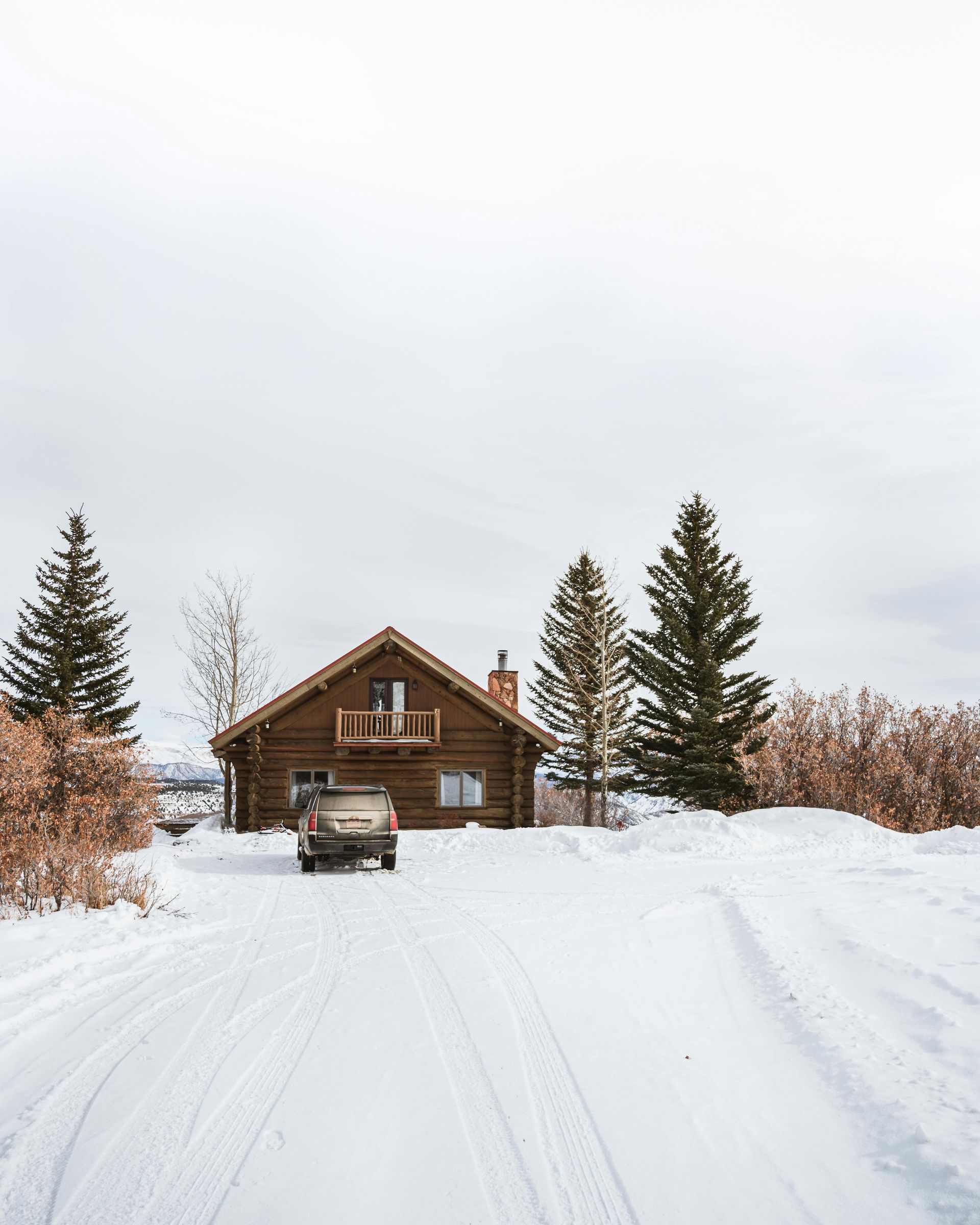 A car is parked in front of a log cabin in the snow.