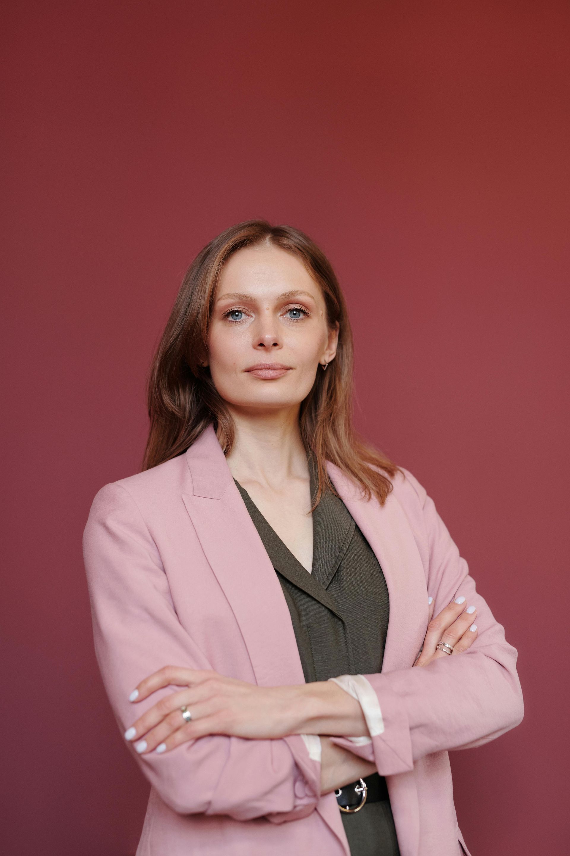 A woman in a pink jacket and green dress is standing with her arms crossed.