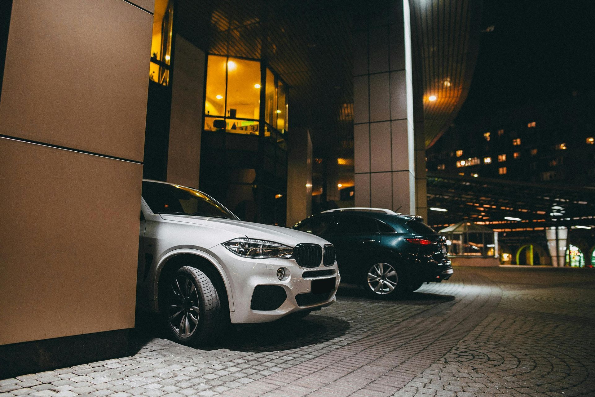 Two cars are parked in front of a building at night.