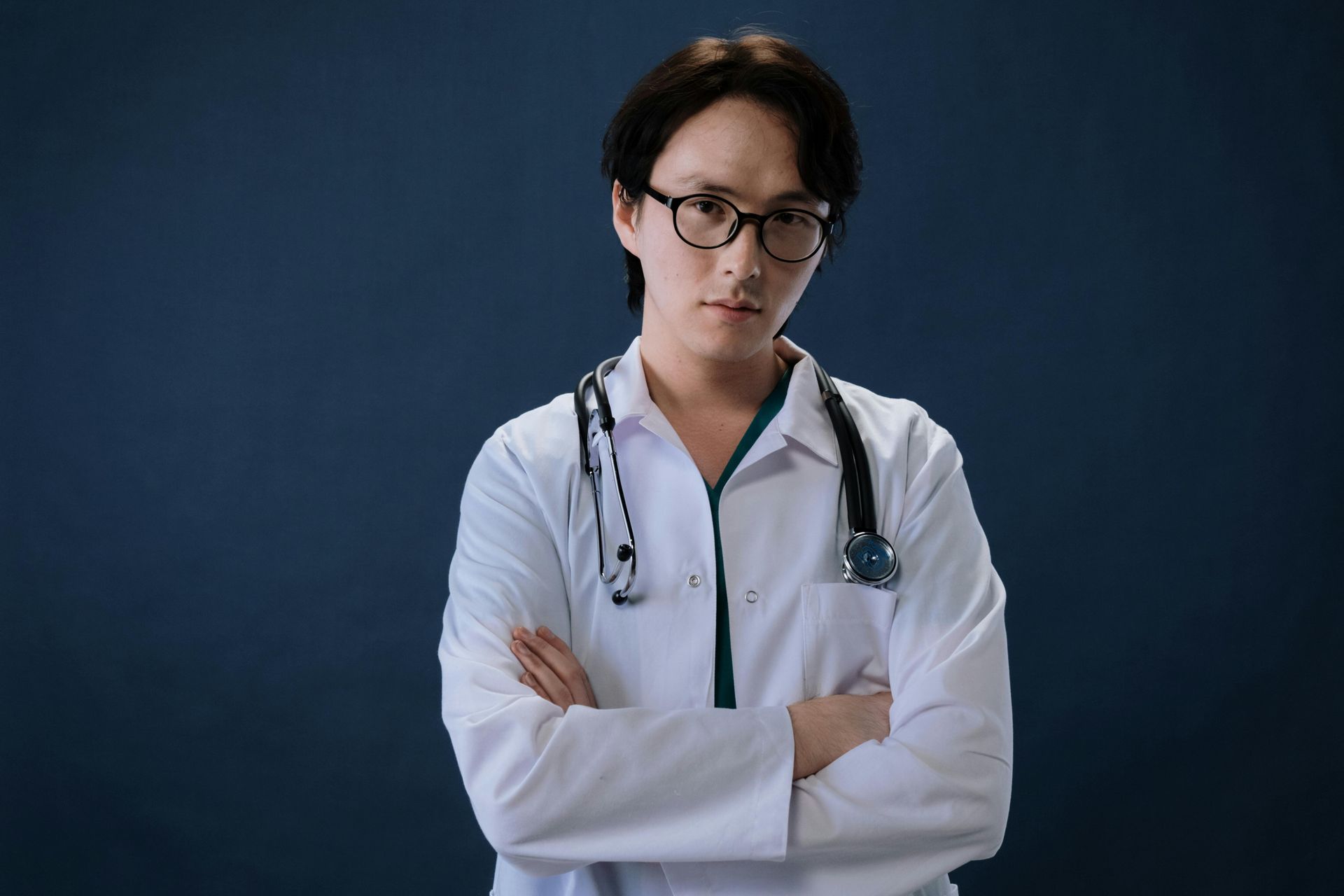 A doctor with a stethoscope around his neck is standing with his arms crossed.