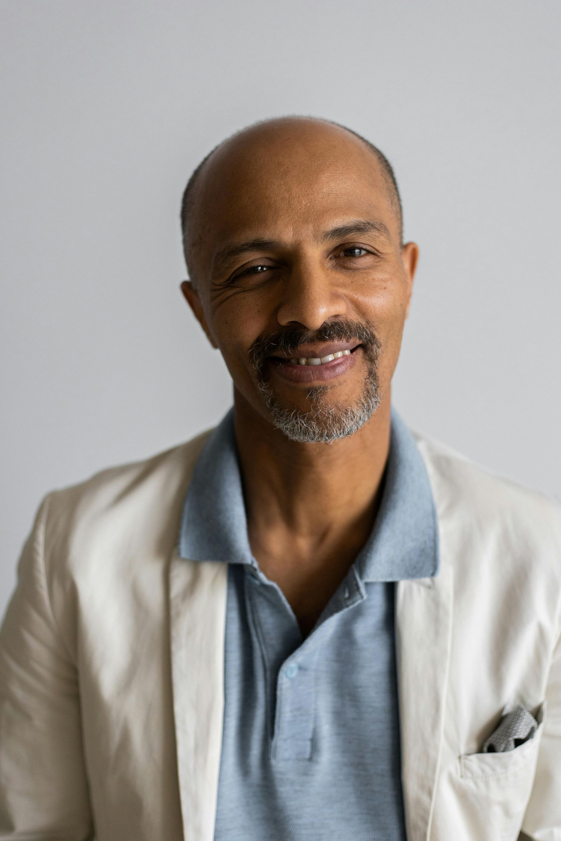 A man with a beard is wearing a white jacket and a blue polo shirt.
