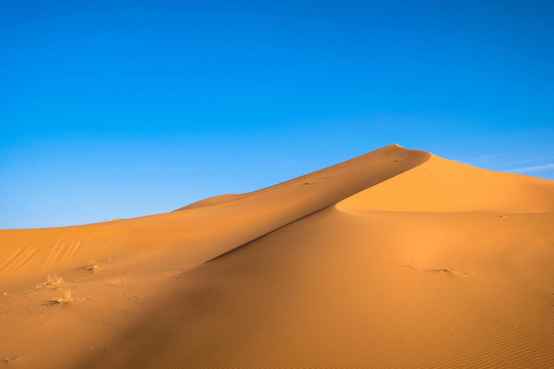 A sand dune in the middle of a desert with a blue sky in the background.