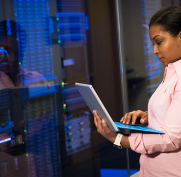 Woman in pink shirt using a laptop, monitoring servers in a data center.