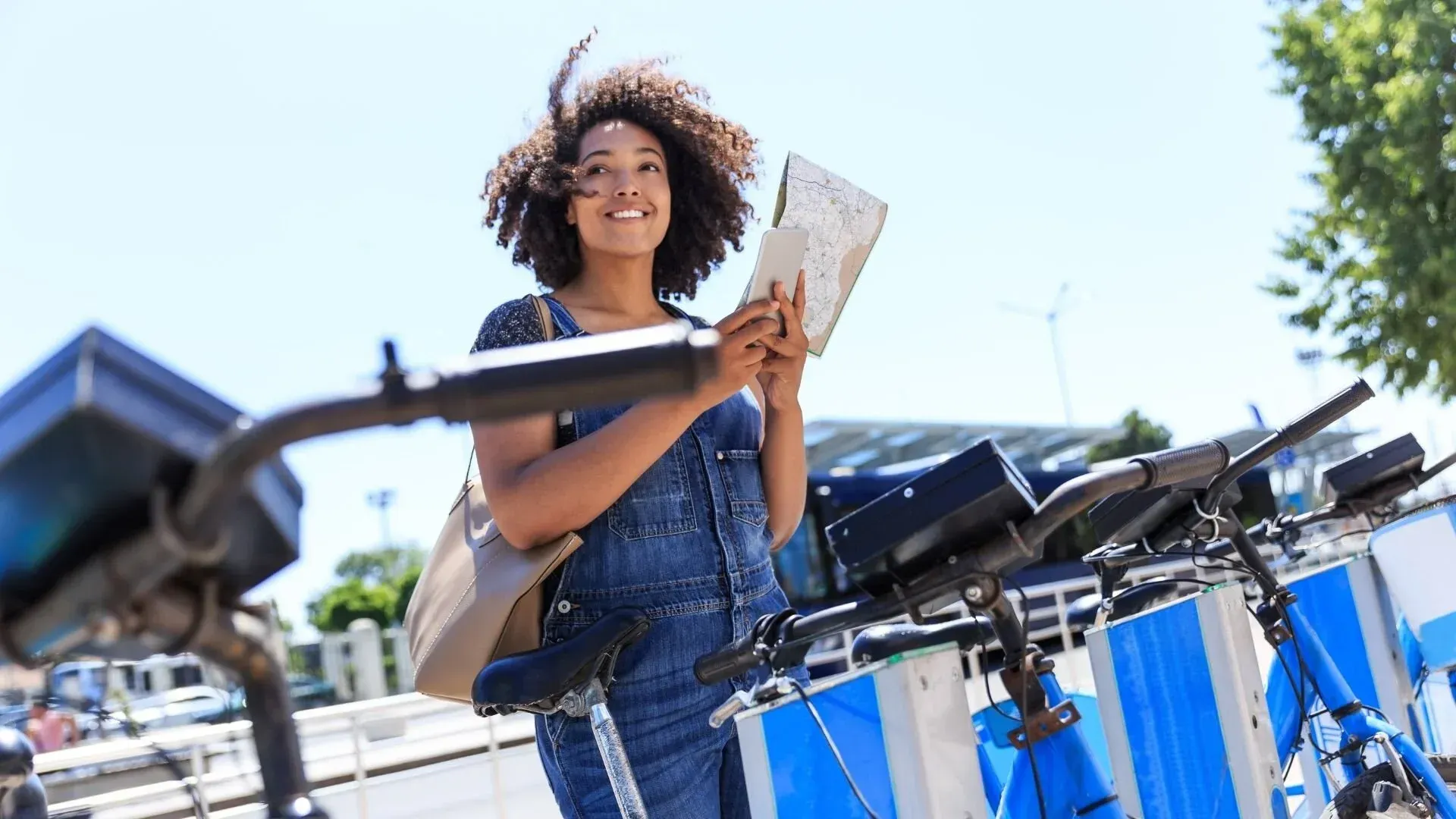 Woman standing by bikes, looking at tablet. Sunny outdoors.