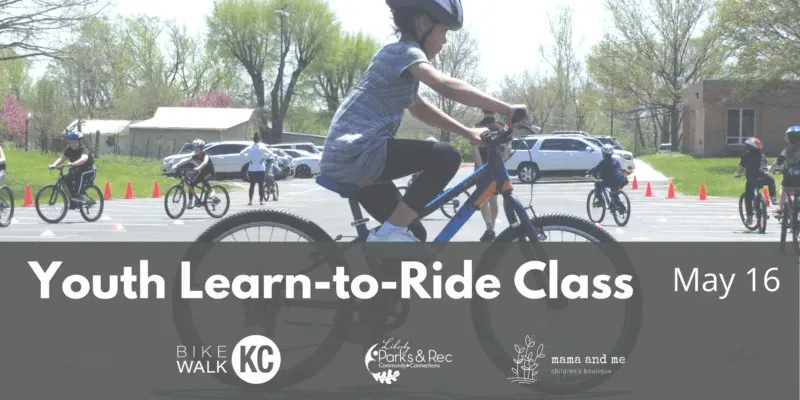 Youths on bikes at a learn-to-ride class. Participants wearing helmets ride on a paved area with a building and parked cars in the background.