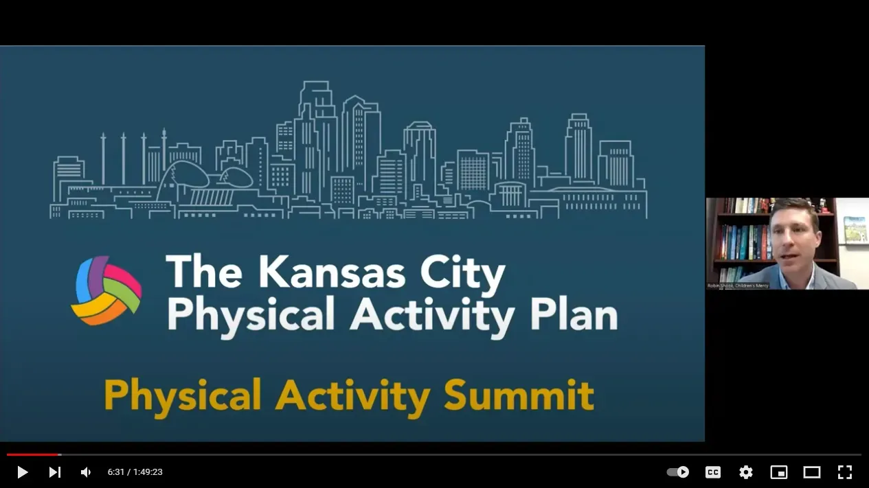 Man presenting at the Kansas City Physical Activity Summit. Kansas City skyline logo on screen.