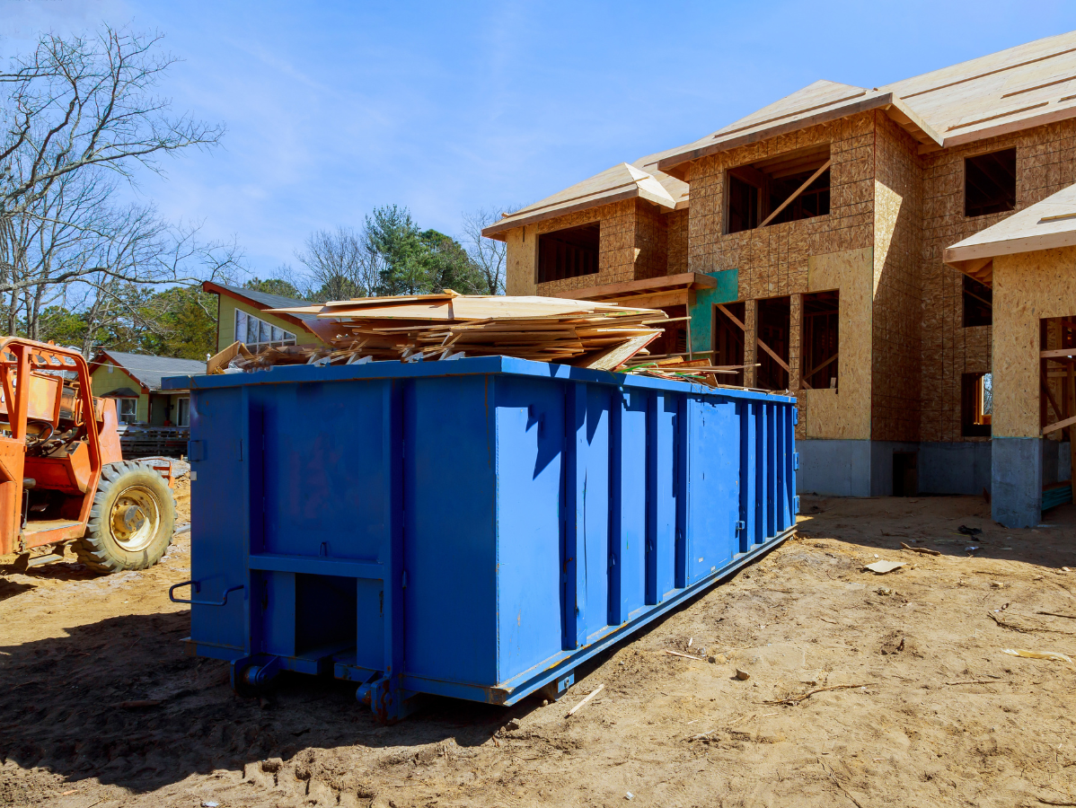 Blue construction dumpster filled with wood debris at a new house construction site.