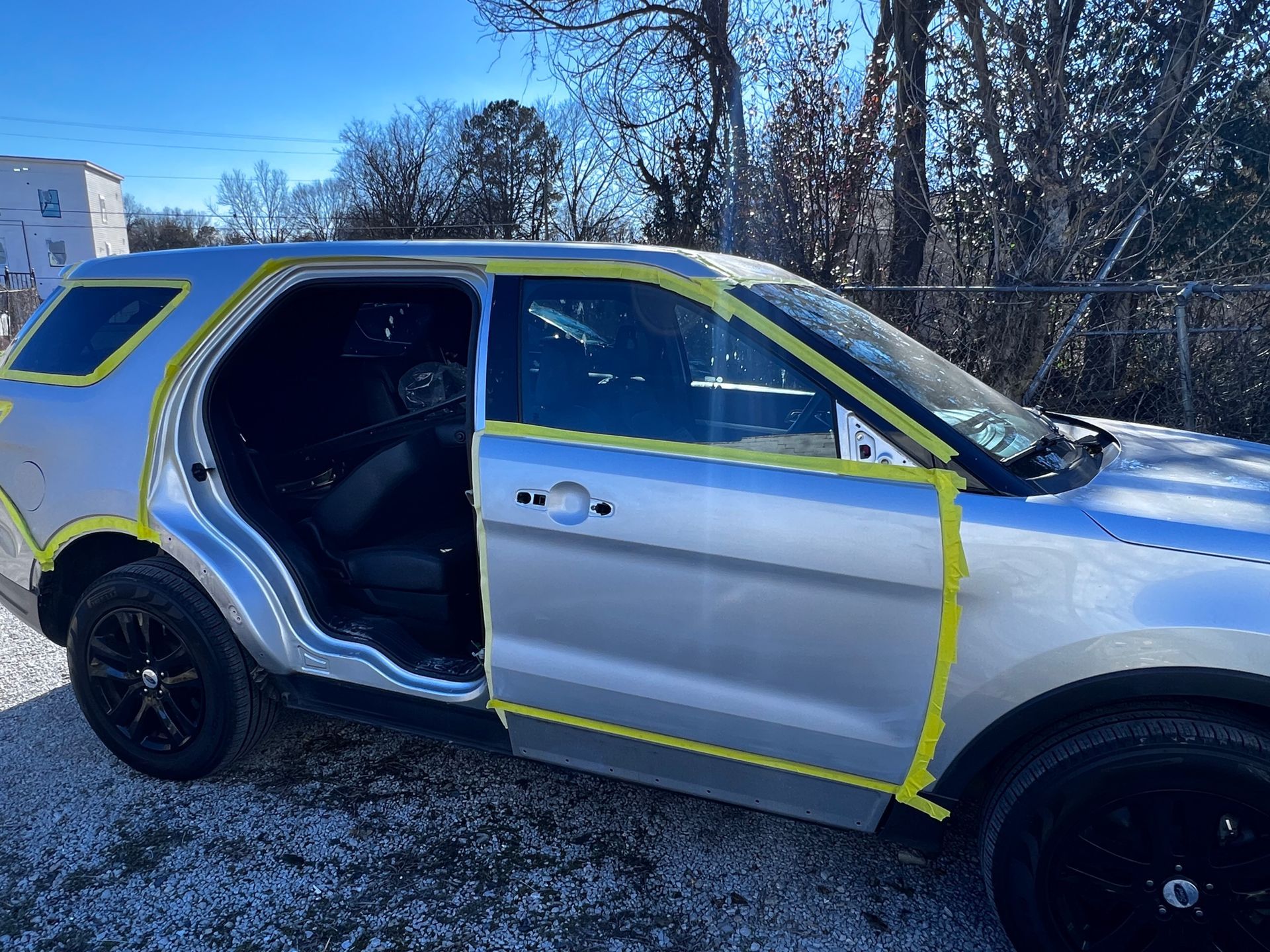 A silver suv with yellow tape on the side is parked in a gravel lot.