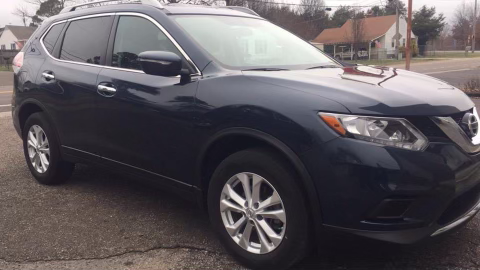 A blue nissan rogue is parked on the side of the road.