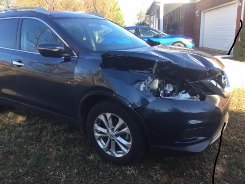 A black car with a damaged hood is parked in front of a garage.