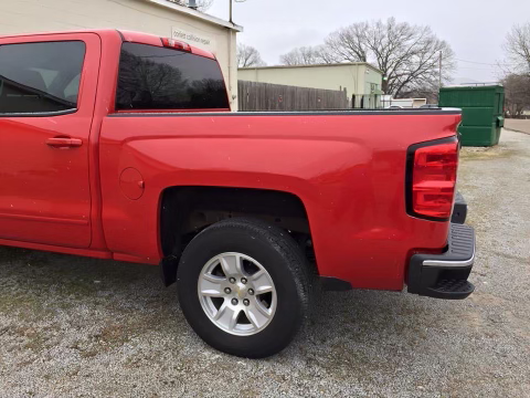 A red truck is parked in a gravel lot in front of a building.