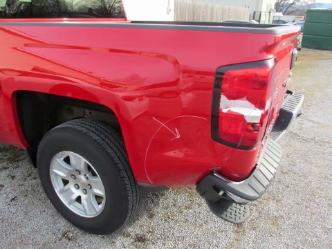 A red truck with a damaged tailgate is parked in a gravel lot.