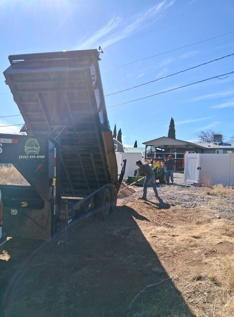 A dump truck is being loaded with dirt in a yard.