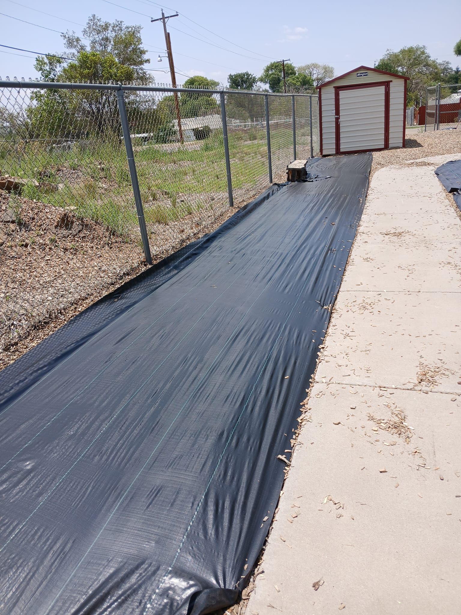 A black tarp is covering a sidewalk next to a fence and a shed.