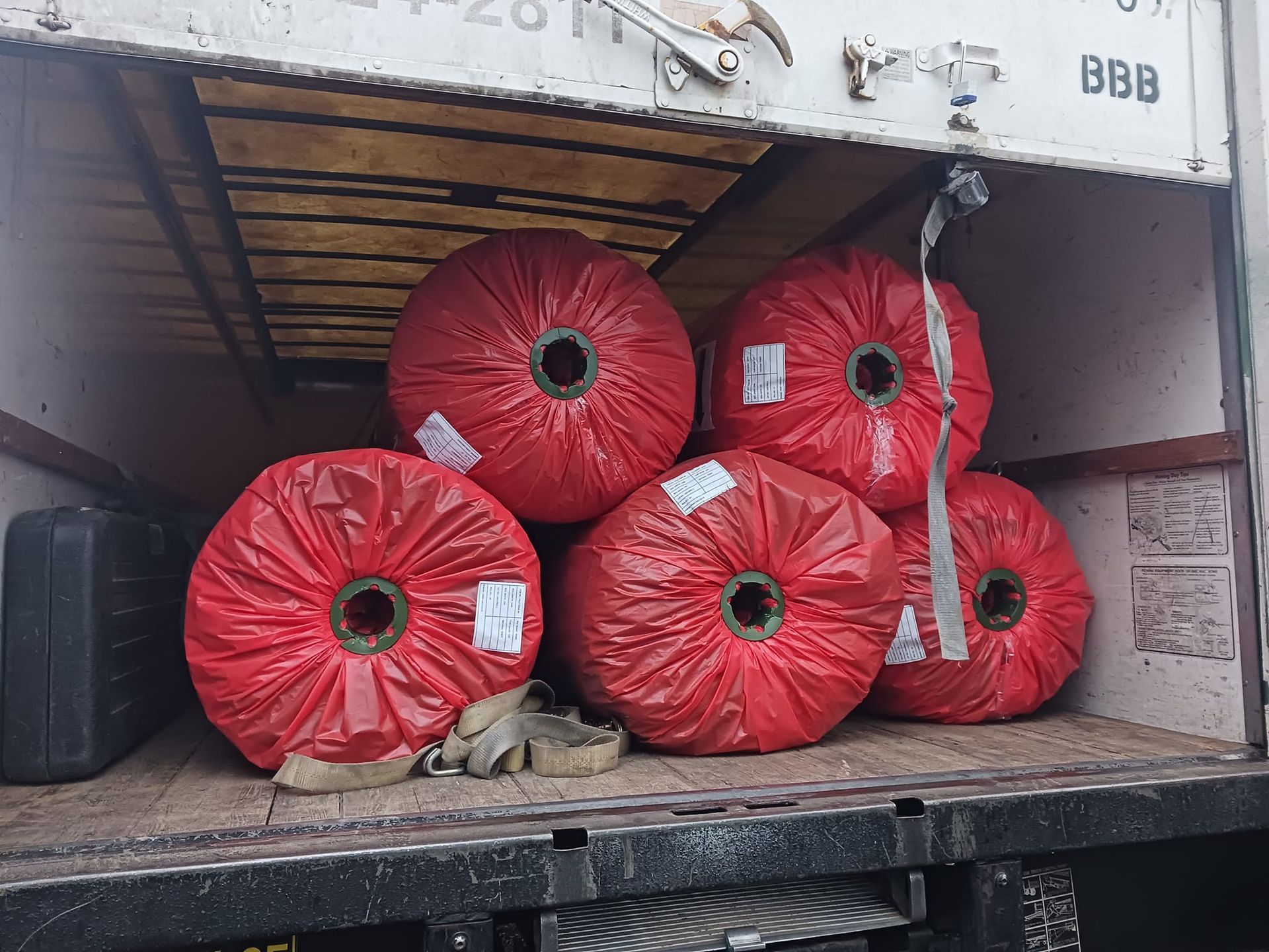 A bunch of rolls of red plastic are stacked on top of each other on the back of a truck.