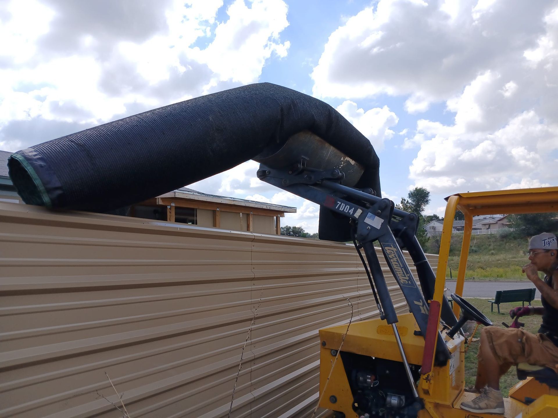 A man is driving a yellow forklift with a hose attached to it.
