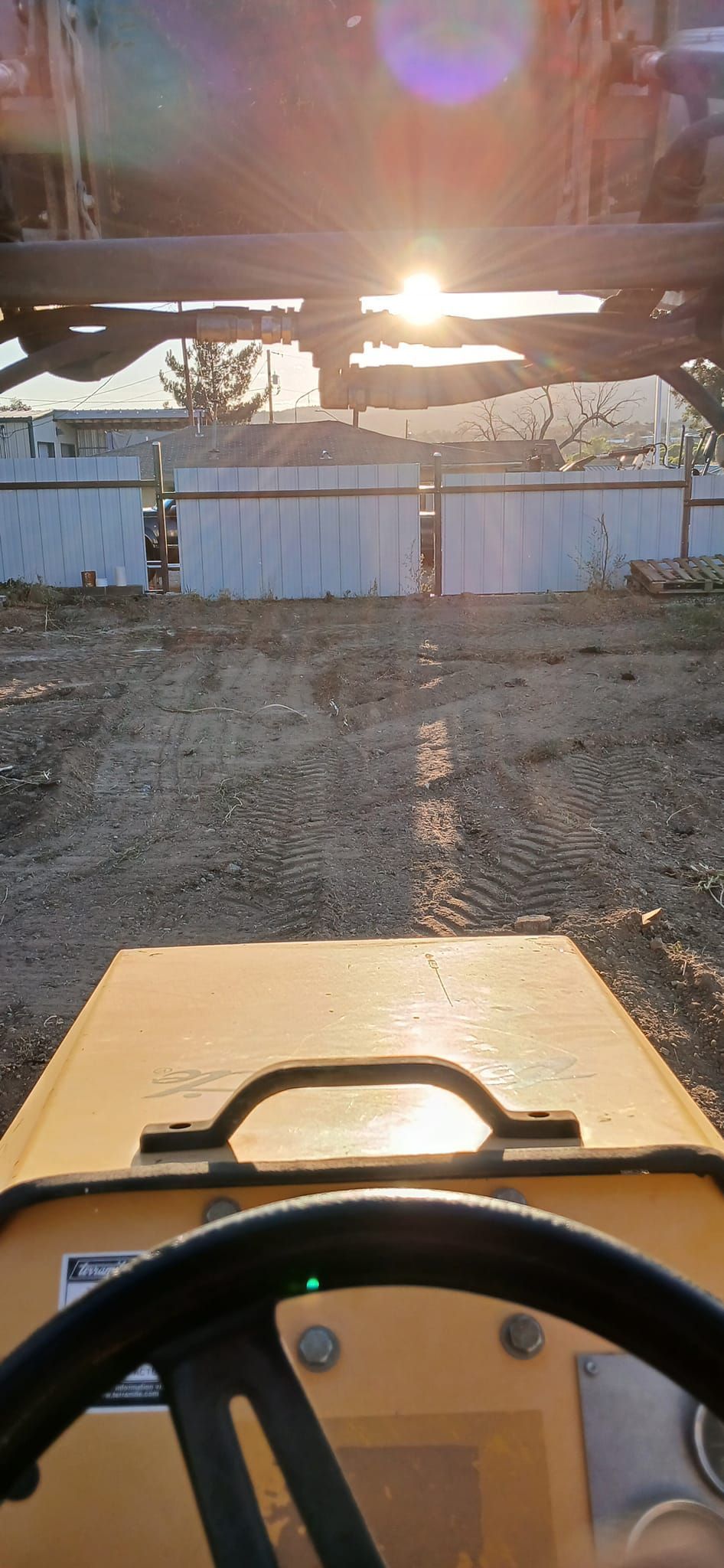A person is driving a yellow tractor on a dirt road.