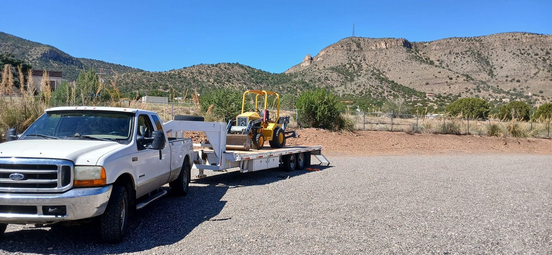 A white truck is towing a trailer with a yellow tractor on it.
