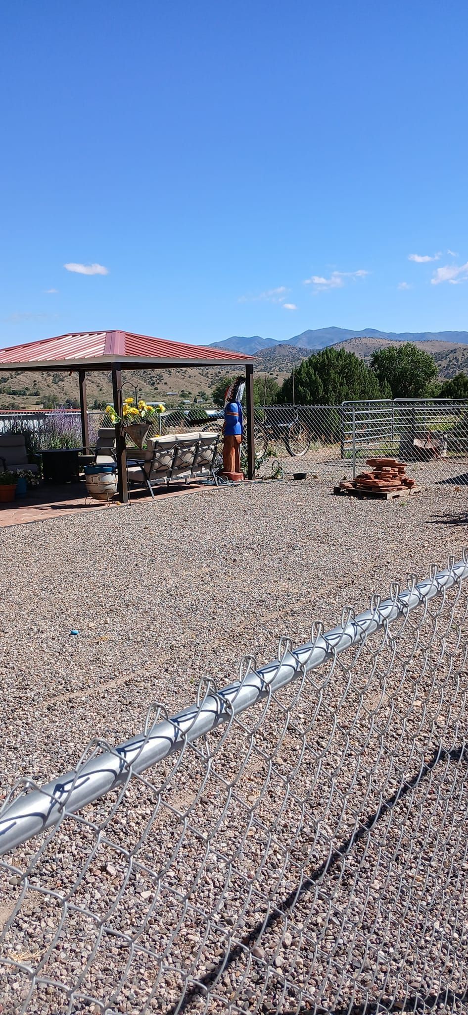 A chain link fence is surrounding a gravel area with a gazebo in the background.