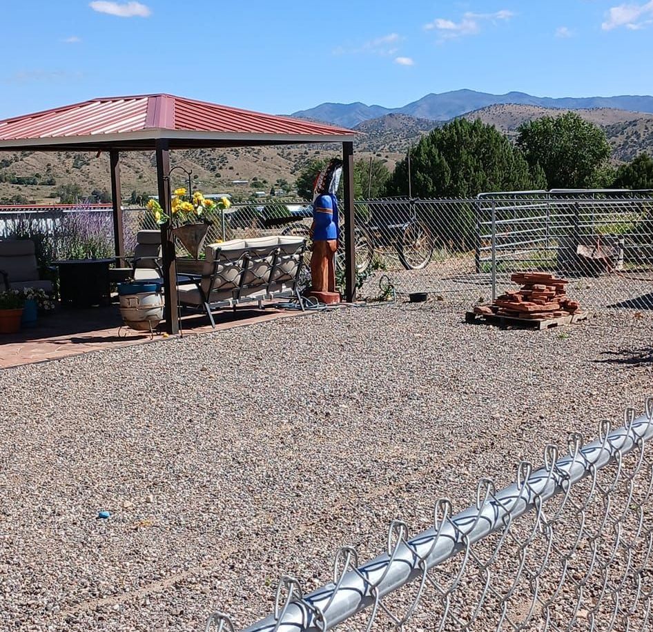 A chain link fence surrounds a gravel area with a gazebo in the background