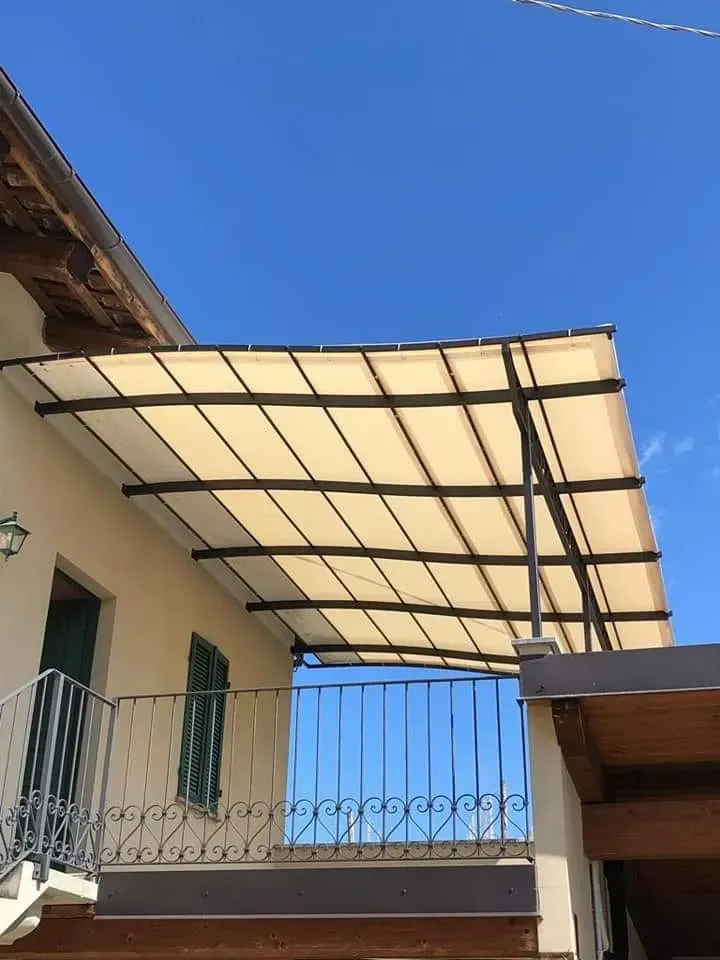 Balcone con tenda da sole beige e struttura in metallo nero contro il cielo azzurro.
