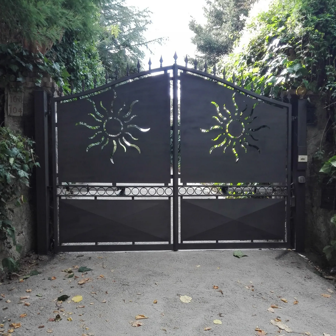 Cancello in metallo nero con ritagli per il sole, che si apre su un vialetto.