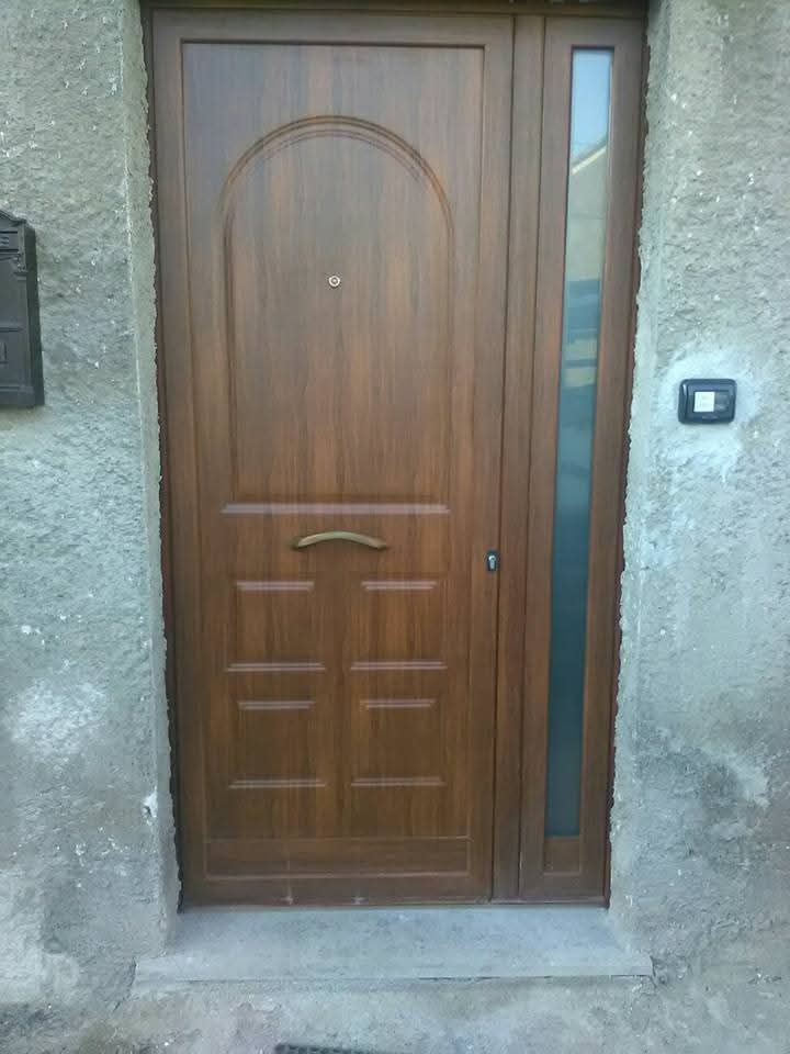 Porta effetto legno marrone con parte superiore arcuata e finestra laterale accanto, inserita in una parete in stucco.