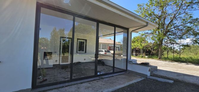 Sala da pranzo con tavolo rotondo, quattro sedie, ampie finestre e lampadario moderno.