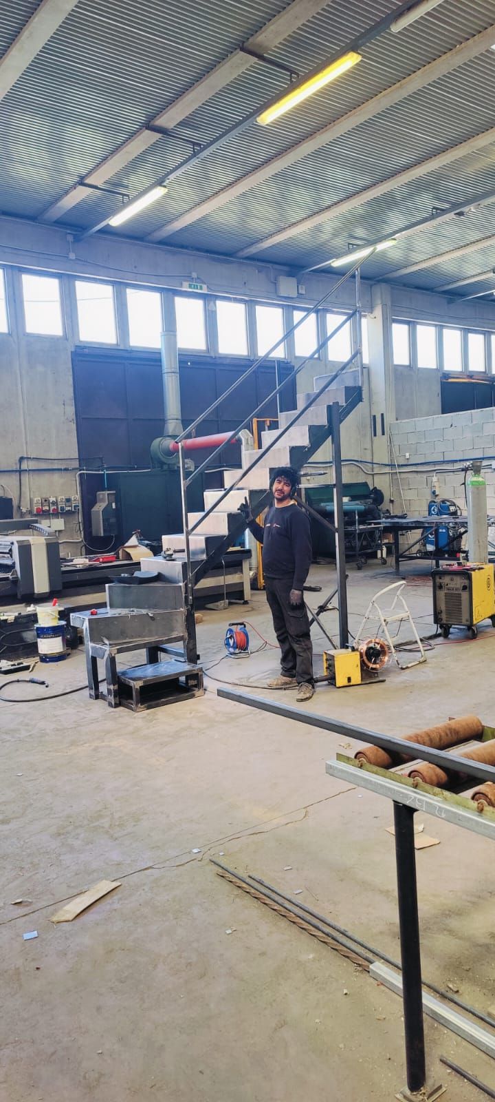 Una persona è in piedi in un'officina. Una scala sale contro un muro e intorno sono sparse attrezzature.