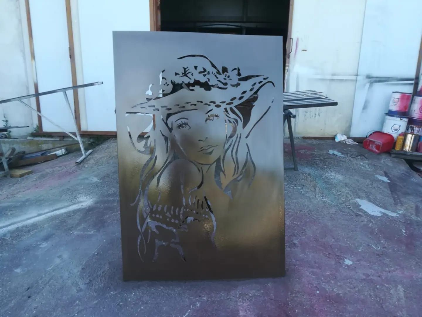 Pannello metallico ritagliato raffigurante una donna con un cappello, esposto all'interno.