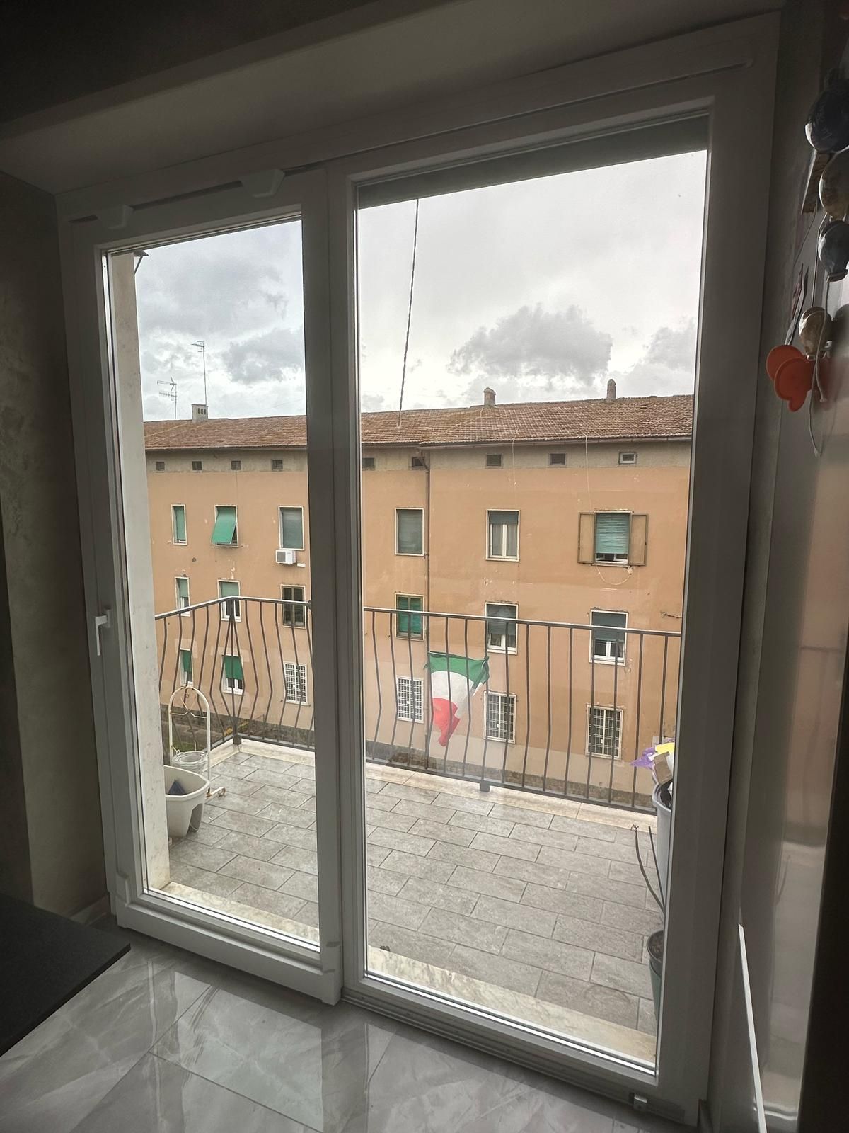 Una finestra con vista su un edificio con balcone e bandiera italiana.