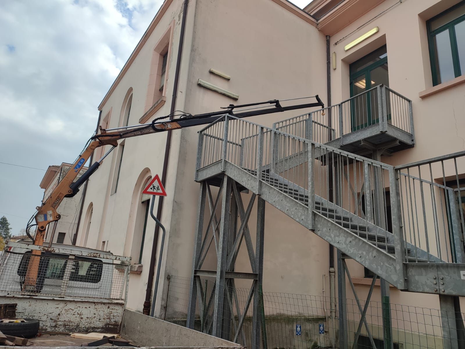 Un camion con un braccio gru vicino a un edificio con una scala esterna in metallo.